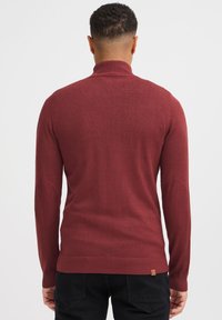 Maglione bordeaux con collo alto, polsini a coste e toppe sui gomiti, caratterizzato da una texture liscia e un design aderente.