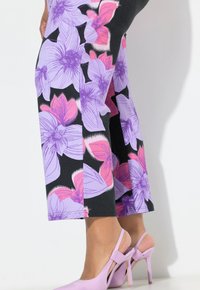 Leggings mit Blumenmuster, die große lila und pinke Blumen auf schwarzem Hintergrund zeigen, mit geradem Bein. Kombiniert mit hellvioletten High Heels.