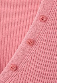 Gros plan sur un tissu côtelé rose avec trois boutons assortis cousus sur un bord tricoté.