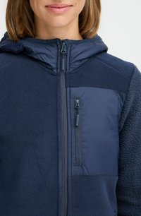 Veste à capuche bleu marine avec un mélange de polaire et de tissu lisse. Elle possède une fermeture éclair à l'avant et une poche zippée sur la poitrine.