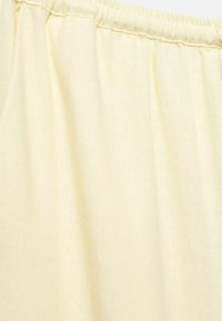 Tissu couleur crème avec une ceinture élastique froncée, montrant la texture et le matériau en maille douce en gros plan.