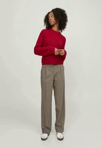 Rød ribbestrikket genser med lange ermer, i kombinasjon med beige høyt liv bukser og hvite casual joggesko. Enkel, moderne design.