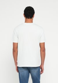 White cotton t-shirt featuring a round neckline and short sleeves, with visible stitching and a small label on the lower side.