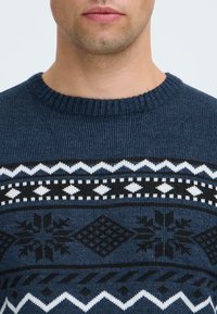Pulover tricotat de culoare bleumarin, cu un yoke decorat într-un model alb-negru, având designuri geometrice și fulgi de zăpadă, cu guler rotund ribat și textură moale.