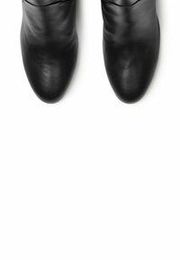 Botas de tobillo de cuero negro con una textura lisa, puntas redondeadas y un sutil detalle fruncido en la parte superior. Diseño limpio sobre un fondo blanco.
