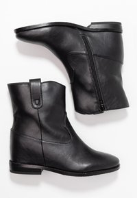 Paire de bottines noires en cuir avec fermeture éclair latérale et talon bas empilé sur fond blanc.