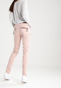 Jasnoróżowe dopasowane spodnie z zamkami błyskawicznymi w kieszeniach, w połączeniu z szaro-białą koszulą o długim rękawie w paski. Gładki materiał i dopasowany design.