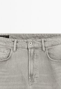 Jeans in denim grigio con un classico design a cinque tasche, dotati di zip e di un bottone argentato in vita. Texture morbida e finitura liscia.