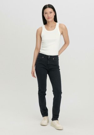 Zwarte denim jeans met vijf zakken, knoopsluiting en lichte stikseldetails. Gecombineerd met een aansluitend wit tanktop en crèmekleurige sneakers.