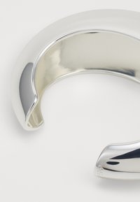 Pulsera de brazalete de plata con una superficie lisa y pulida, que presenta un diseño abierto y bordes redondeados. Destaca por su acabado brillante y su estructura sin costuras.