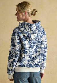 Bluza z kapturem w niebiesko-białym wzorze toile, miękka w dotyku, z ribbowymi mankietami i dołem, zestawiona z dżinsami.