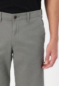 Gray cotton trousers featuring a straight cut, front pocket, and button closure. The fabric has a smooth texture with subtle stitching details.