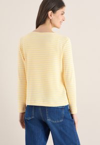 Haut à manches longues rayé jaune et blanc avec un col rond et une texture côtelée, porté avec un jean en denim bleu.