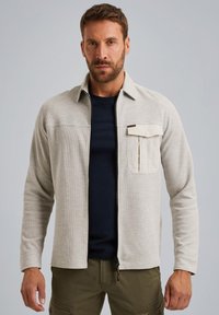 Lichtgrijs, gestructureerd jack met een rits aan de voorkant, puntkraag en een borstzak. Draag het over een donkerblauw shirt, gecombineerd met kaki broek.