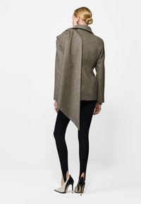 Brązowa kurtka z wełny z asymetrycznym krojem, z pojedynczym kołnierzem i długimi rękawami, połączona z czarnymi legginsami i dwukolorowymi szpilkami.