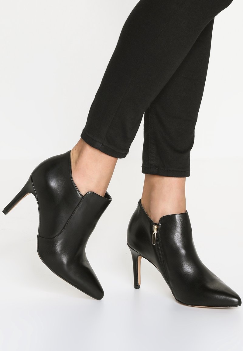 Stivaletti alla caviglia in pelle nera con punta appuntita, tacco alto e dettaglio con cerniera laterale. Finitura strutturata con un design elegante e moderno.