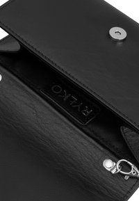 Billetera de cuero negro con cierre de botón a presión, bolsillo interior con cremallera, superficie texturizada y etiqueta de marca visible. Accesorios en plata.