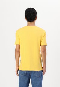 Tricou galben cu mânecă scurtă, fabricat din bumbac moale, având un guler clasic și o croială relaxată, cu cusături vizibile pe tiv.