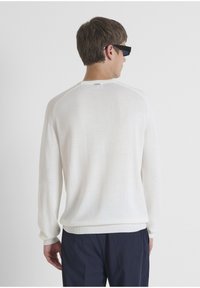 Witte gebreide trui met lange mouwen, geribbelde halslijn en gestructureerde schouderdetails; gecombineerd met marineblauwe broek.