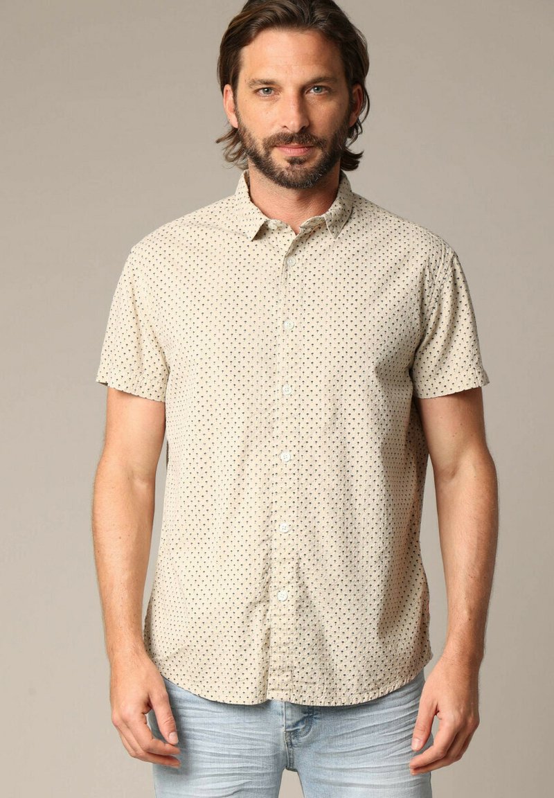 Chemise à manches courtes à boutons en beige avec un léger motif à petits pois noirs, fabriquée en tissu léger, dotée d'un col classique et d'une coupe décontractée.