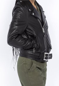 Svart läderbikerjacka med silverdetaljer, sned dragkedja, bred krage och bälte i midjan. Slät textur med minimala detaljer.