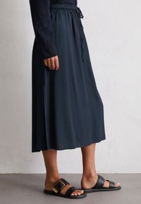 Marinefarbene Midi-Rock mit elastischem Bund und Kordelzug. Glatte Textur, Seitenschlitze, kombiniert mit schwarzen Sandalen mit goldener Schnalle.
