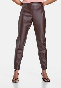 Bruna läderbyxor med en figurnära design, featuring en hög midja, subtila sömmar och avsmalnande ben. Slät textur och elegant finish.