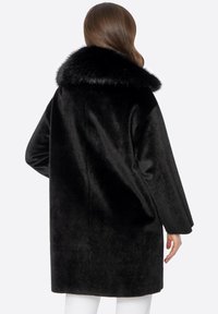 Abrigo de piel sintética negra con un amplio cuello, silueta recta y mangas largas. Textura suave con un acabado mullido, diseño a la altura de la rodilla.
