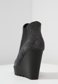 Stivaletti con tacco a cuneo in suede grigio scuro con una texture liscia, pannelli laterali elastici e una suola in gomma nera spessa.