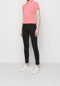 Różowa koszulka polo z dzianiny warkoczowej, czarne dopasowane jeansy oraz białe trampki. Koszulka ma kołnierzyk i logo, a jeansy klasyczne kieszenie.