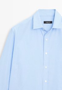 Camicia azzurro chiaro con sottili righe bianche verticali, colletto a punta e bottoni bianchi. Tessuto liscio con una consistenza croccante.