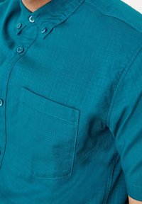 Camicia azzurra a maniche corte con colletto button-down, tessuto testurizzato e una tasca sul petto. Include bottoni coordinati.
