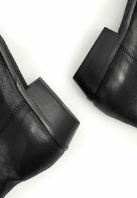 Botas de tobillo de cuero negro con una superficie texturizada y tacones de bloque redondeados que presentan acentos mate y brillantes en contraste.