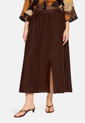 Femme portant une jupe midi marron avec une fente à l'avant, associée à des sandales à talons marron et un haut multicolore à motif de feuilles.