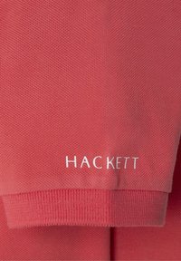 Korala polo majica od teksturiranog materijala, sa rebrastim ovratnikom i manžetama. "HACKETT" logo u srebrnoj boji na lijevoj rukavu.