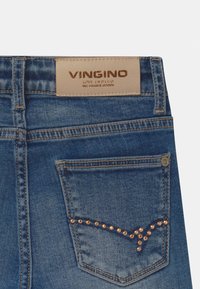 Blaue Denim-Jeans mit einem beigen Lederbundlabel, verziert mit dekorativen goldfarbenen Nieten auf der Gesäßtasche. Klassisches Fünf-Taschen-Design.
