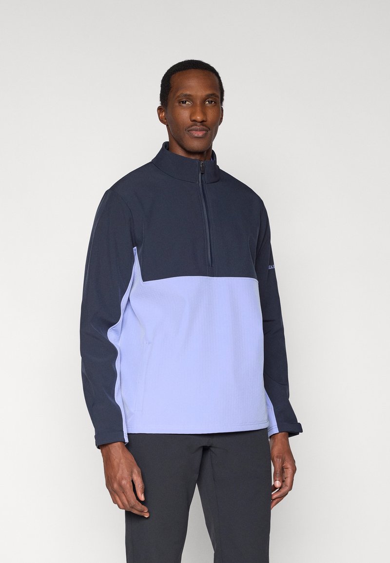 Pulover cu fermoar de un sfert în nuanțe de bleumarin și lavandă deschisă; are mâneci lungi, guler înalt și material texturat pentru izolație.