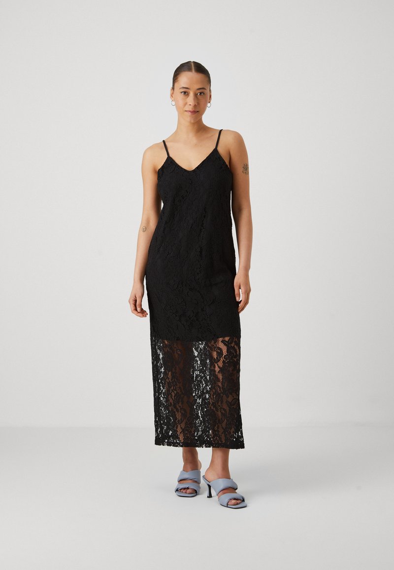 Μαύρο δαντελένιο φόρεμα με λεπτές τιράντες, διαθέτει φαρδιά σιλουέτα και διαφανές, κα patterned κάτω μέρος. Συνδυάζεται με ανοιχτό μπλε σανδάλια με τακούνι.