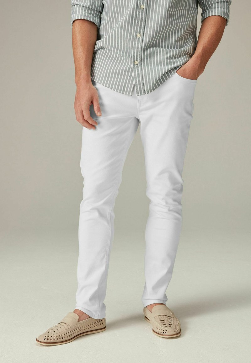 Witte op maat gemaakte broek gecombineerd met een licht gestreept overhemd met knoopsluiting. Beigekleurige loafers met vlechtdetail maken de outfit compleet.
