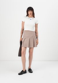 White short-sleeve top with a blue tag, paired with a brown pleated mini skirt. Black loafers and a brown handbag complete the look.