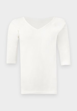 Λευκό μακρυμάνικο μπλουζάκι με V λαιμόκοψη και εφαρμοστή γραμμή, απλωμένο επίπεδα σε γκρι ανοιχτό φόντο.