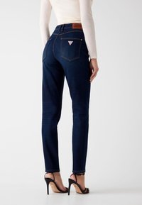 Donkere denim jeans met een slim fit, voorzien van achterzakken, een taille op middenhoogte en een bruin leren label. Draag ze met zwarte sandalen met hoge hakken.