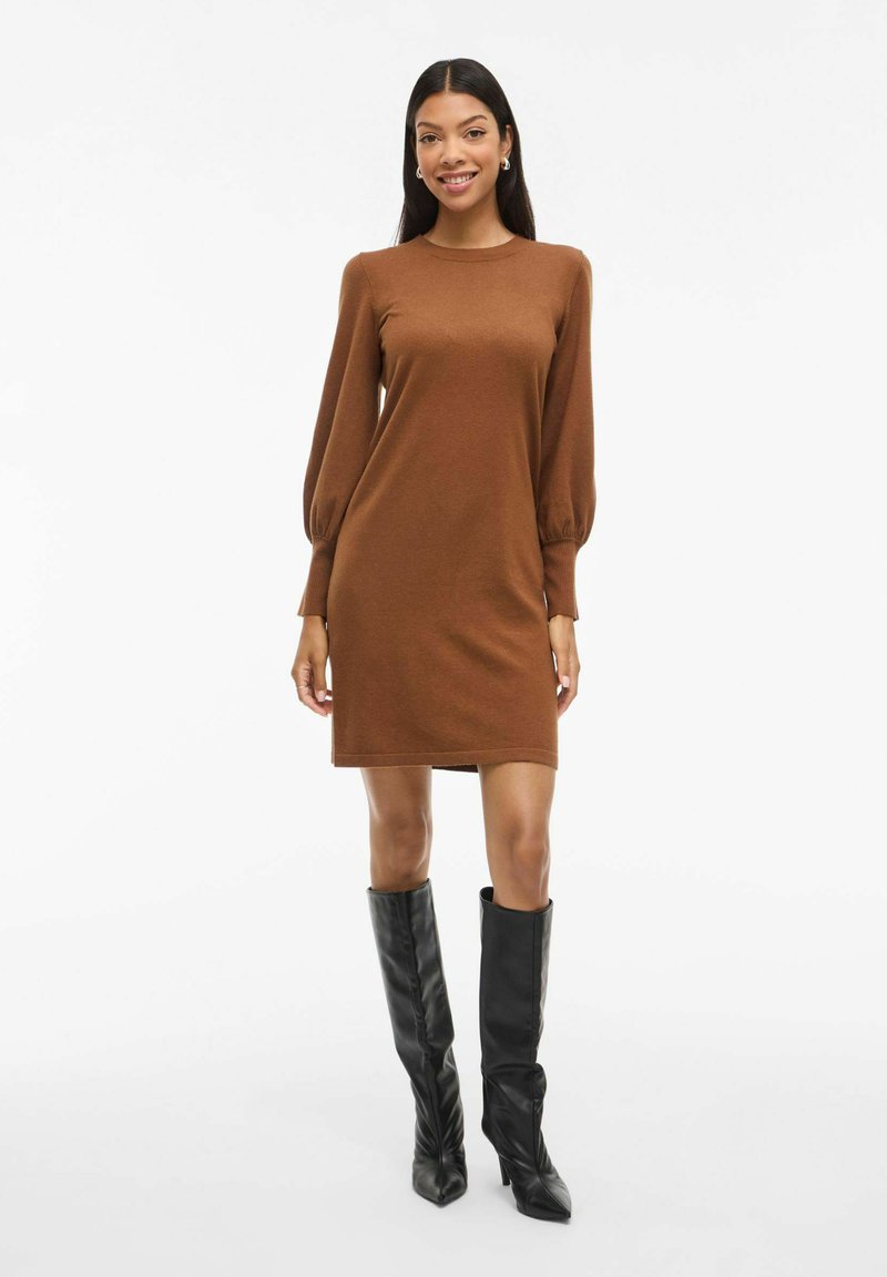 Robe en tricot marron à manches bouffantes longues et encolure ronde, assortie à des bottes noires jusqu'aux genoux ; texture lisse, silhouette droite.