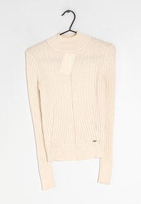 Pull beige clair côtelé à manches longues avec un col montant, présentant un motif texturé et un petit logo près de l'ourlet.