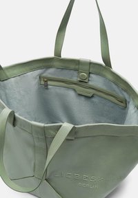 Grüne Ledertasche mit glatter Textur, ausgestattet mit einer inneren Reißverschlusstasche und einer Markeninschrift. Robuste Griffe zum Tragen.