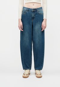 Løse blå denimjeans med en lys vask, fem lommer og lukning med knap. Parret med beige sneakers med et subtilt mønster.
