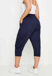 Marinblå beskurna byxor med elastisk midja, fickor och en något lös passform. Matchas med vita sneakers för en avslappnad stil.