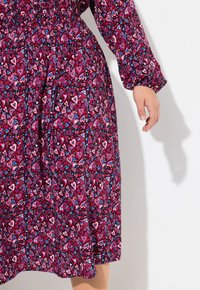 Vestido morado con un diseño de corazones en rosa, rojo y azul. Presenta mangas largas y una banda elástica en la cintura para un efecto fruncido.