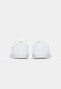Hvite sneakers med en glatt lærfinish. Har et gulllogo og øyestrammere, polstret krage og flat hvit gummisåle.