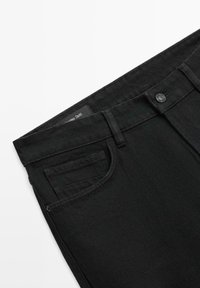 Czarna dżinsowa talia spodni z widocznym guzikiem, szlufkami na pasek, przednią kieszenią oraz małą kieszonką na monety na białym tle.